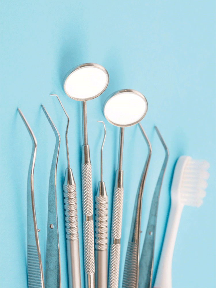Assorted dental instruments on a light blue surface, including two round dental mirrors, pointed probes, curved tweezers, and a white toothbrush.