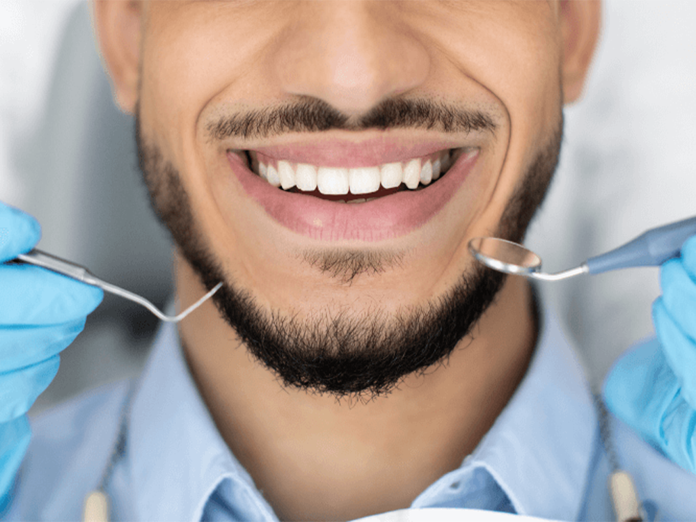 man-smiling-with-dental-pick-and-mirror-next-to-his-face